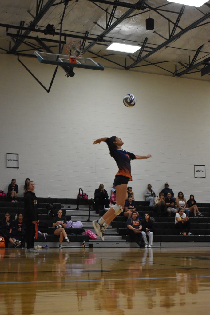Varsity Player Macayla jump serving, picture of her in midair about to make contact with ball 