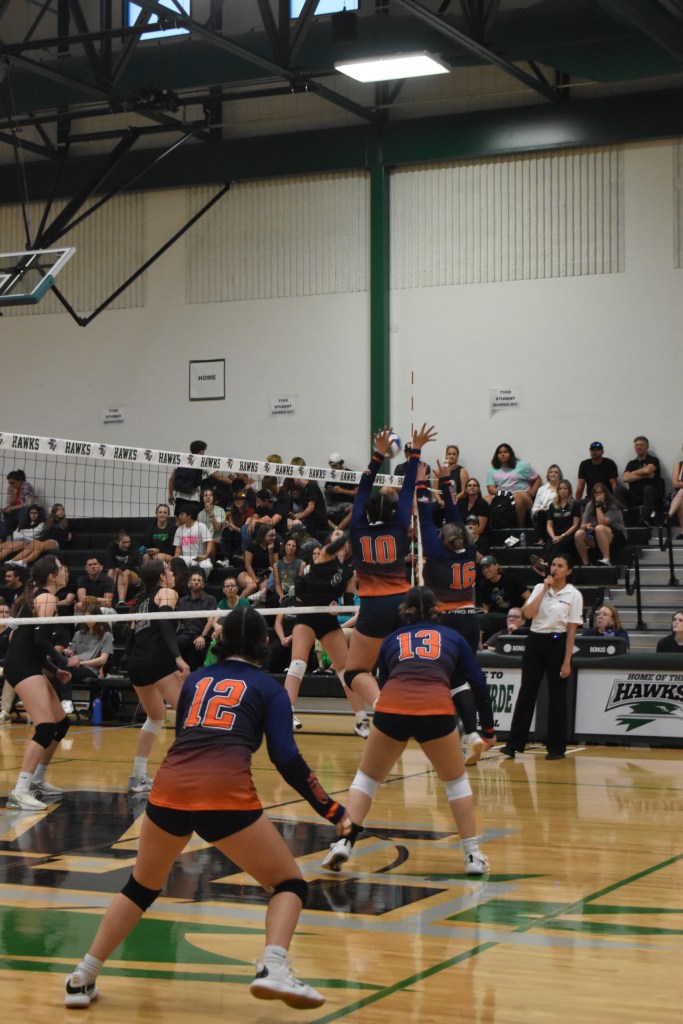 Two varsity players (Divina and Brianna) in midair making a block. with two other players down and ready