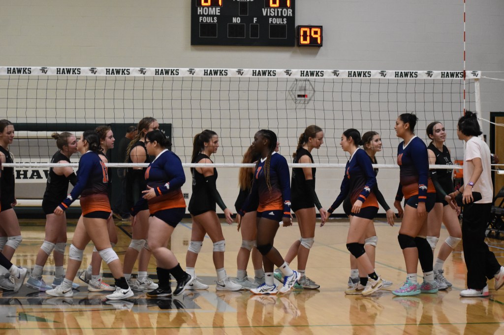 Varsity players handshake opposite team under net congratulating other team  