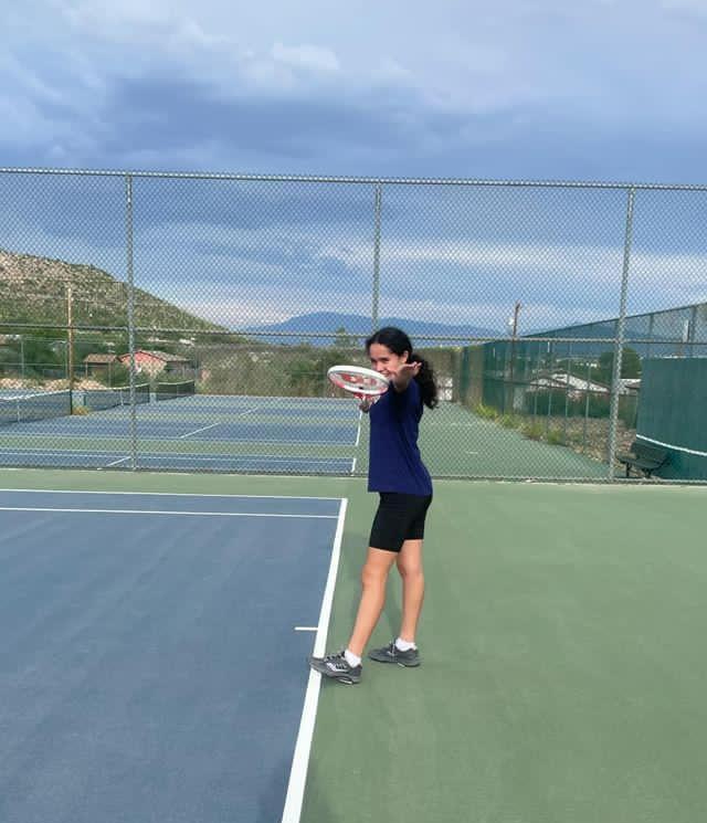 girl posing with tennis racquet on tennis court on a cloudy day