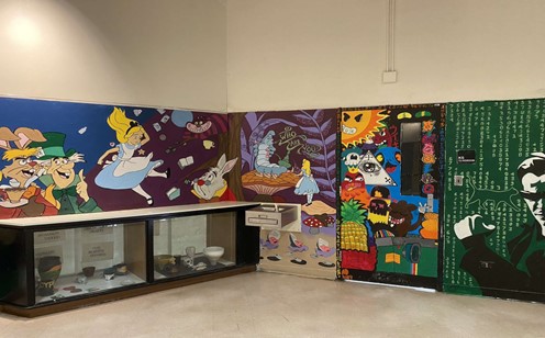 Landscape picture shows multiple murals of characters: Alice in Wonderland, The Matrix, as well as graffiti art. 