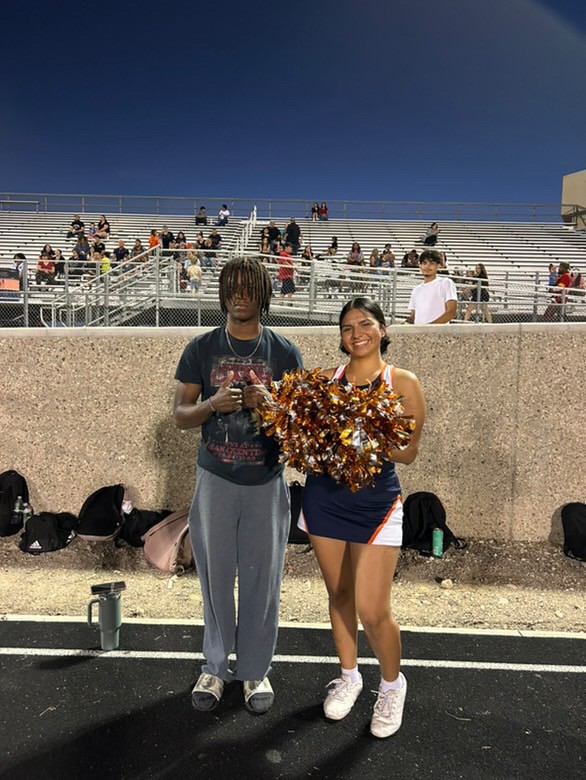  Cheerleader posing with football player on track during varsity football game.