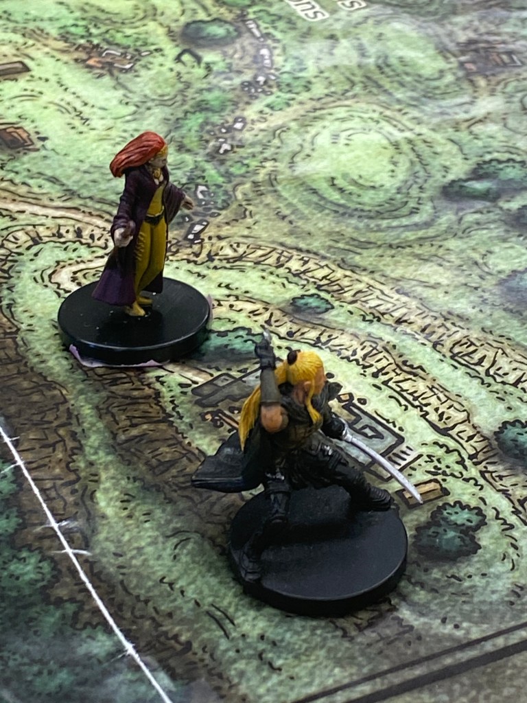 Zoom in photo of character props facing the right with the D&D board (mostly green) under it. 